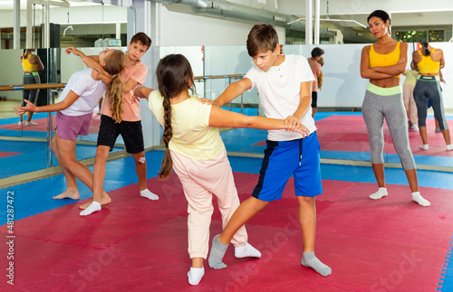 Sporty girls and boys are practices self-defence moves in pairs in sporty gym