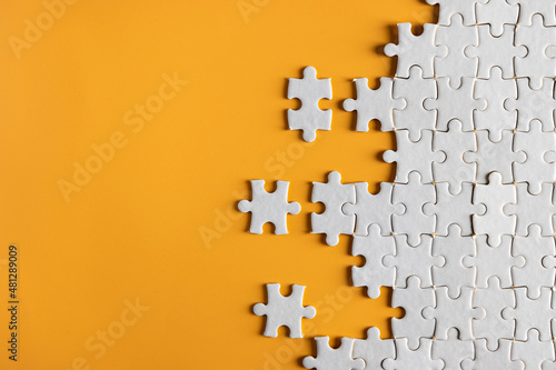 top view of white unfinish jigsaw puzzle on yellow orange background. business concept.
