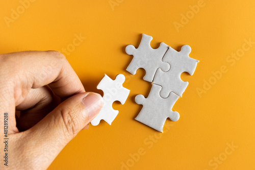 top view of hand holding a piece of jigsaw puzzle. white jigsaw puzzle on yellow or orange background. problem solving , business concept