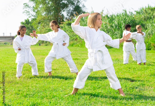 Schoolgirl eight years old in kimono with white belt exercising karate at summer park