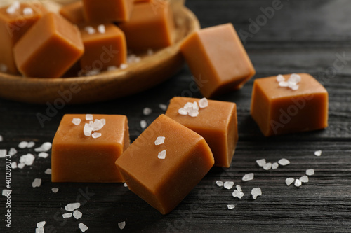 Yummy caramel candies and sea salt on black wooden table, closeup photo