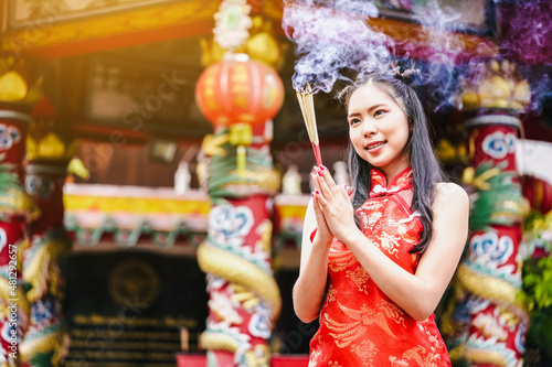 Asian women wearing cheongsams light incense sticks to pray to the gods for blessings on Chinese New Year.