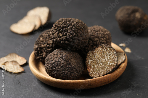 Black truffles in wooden plate on grey table, closeup photo