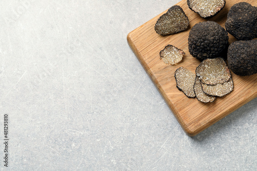 Black truffles with wooden board on light grey table, top view. Space for text