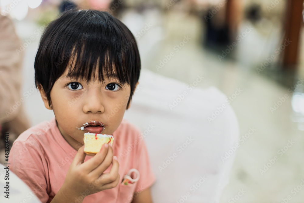 Cute little boy is eating cake while looking at the camera Cute little boy is eating cake while looking at the camera