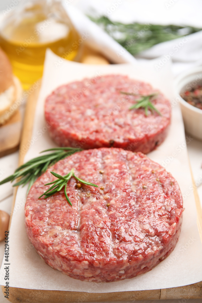 Raw hamburger patties with rosemary on wooden board, closeup Raw hamburger patties with rosemary on wooden board, closeup