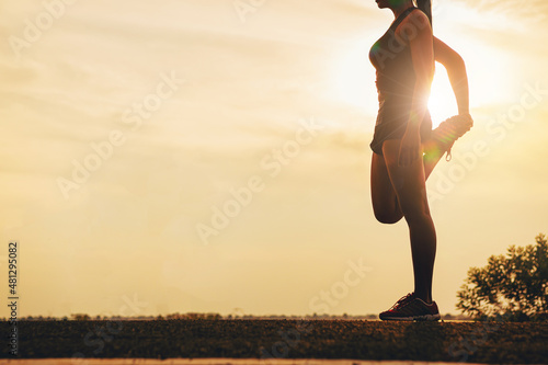 Silhouette of young woman warming up, stretching her muscle at the road track sunset. Fit runner workout and warming up with sunset background.