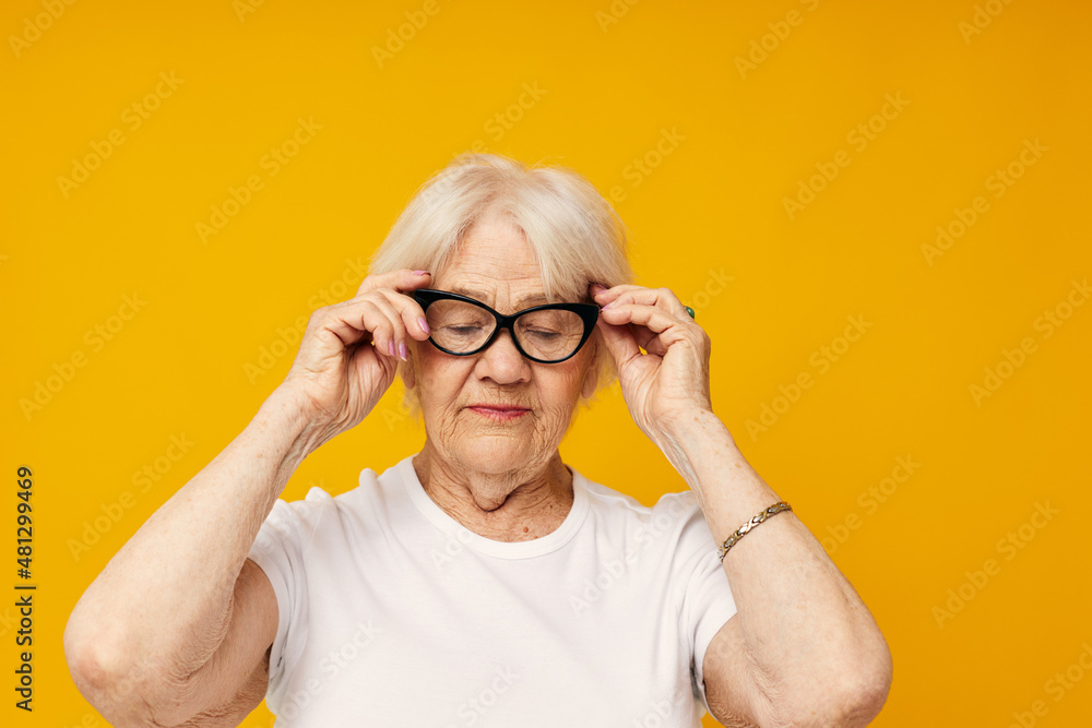 elderly woman in a white t-shirt wears glasses yellow background elderly woman in a white t-shirt wears glasses yellow background