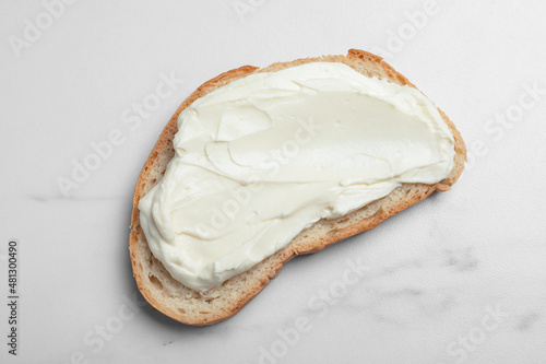 Slice of bread with tasty cream cheese on white marble table, top view photo