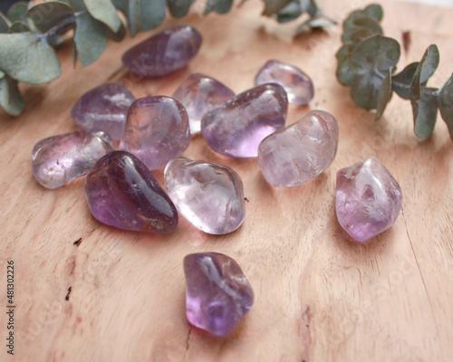 фотографія Amethyst crystal tumbled stone, smooth purple rock on wood with leaves