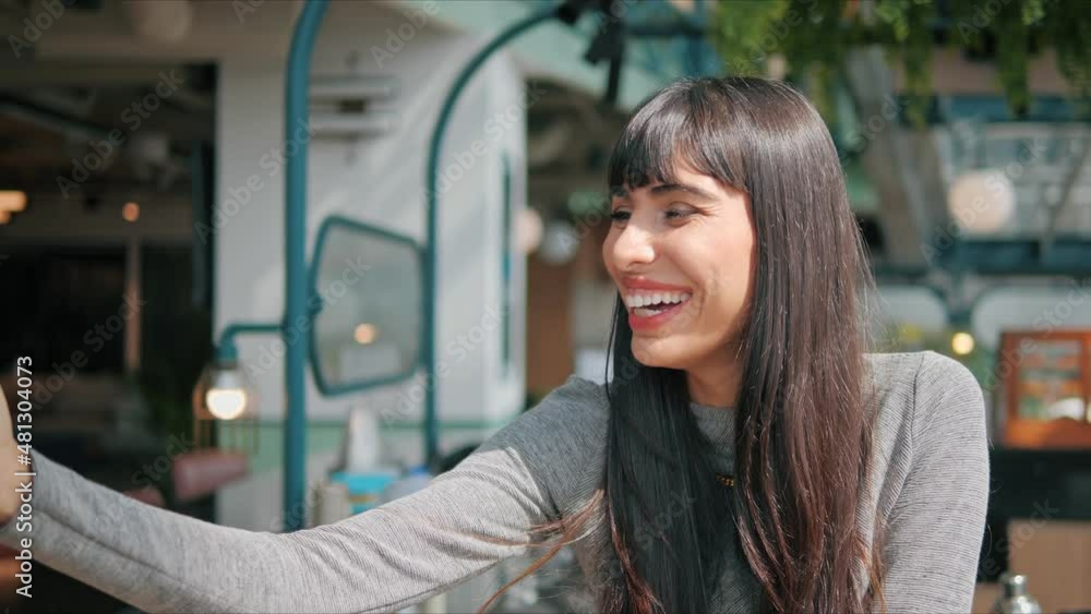 A young woman is on the phone with someone via video call. She speaks cheerfully and with a smile on his face in restaurant A young woman is on the phone with someone via video call. She speaks cheerfully and with a smile on his face in restaurant