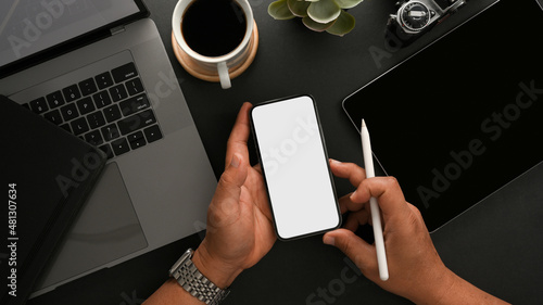 Top view of a male's hands holding a smartphone mockup on working table.