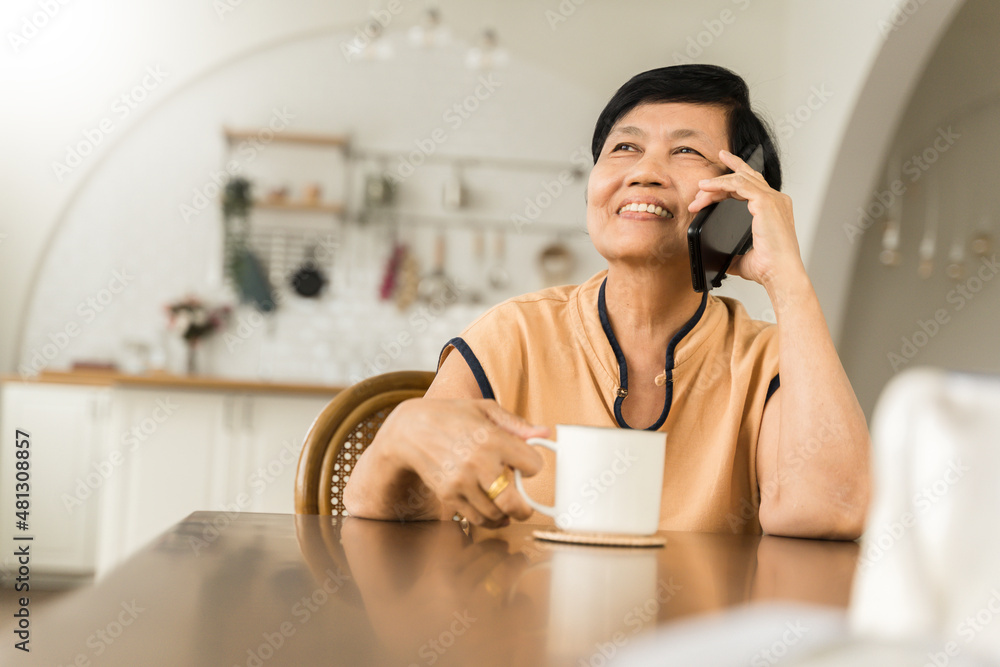 Happy Asian senior adult woman talking on smartphone sitting at table, Mature Female using mobile phone Happy Asian senior adult woman talking on smartphone sitting at table, Mature Female using mobile phone