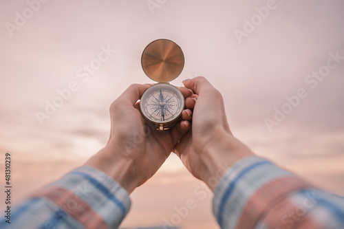 Unrecognizable woman holding a vintage compass in the background of the sunset sky.