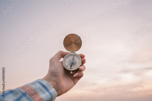 Vintage compass in the hands of the traveler against the sky during sunset.