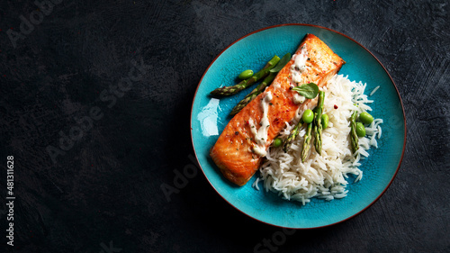 Baked salmon with rice and asparagus on gray background.