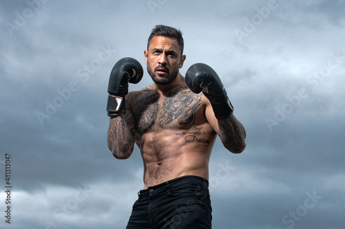 Sport boxing. Sportsman boxer fighting on sky background. Strong athletic man with boxing gloves punching. Muscular boxing man.
