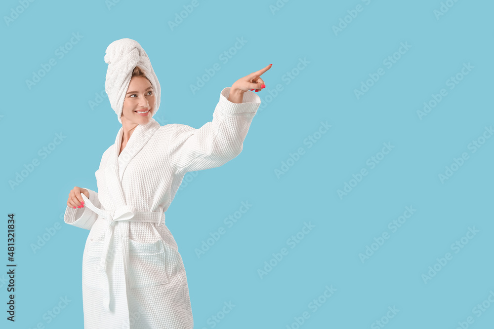 Pretty young woman in bathrobe pointing at something on blue background Pretty young woman in bathrobe pointing at something on blue background