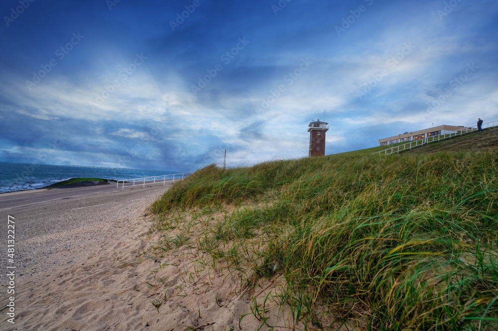 Landscape, seascape with spectacular sunset on the coast of Huisduinen. Sand and grass, behind it the Lange Jaap lighthouse. Colorful landscape and seascape. postcard, card, greeting card