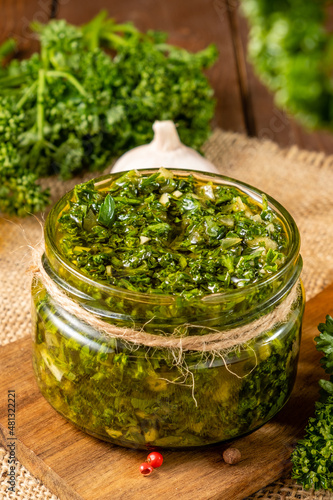 Traditional Argentine chimichurri sauce in a glass jar on a wooden board.
