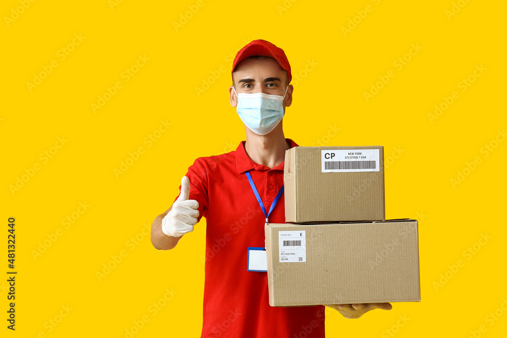 Male courier in medical mask and with parcels showing thumb-up on color background Male courier in medical mask and with parcels showing thumb-up on color background
