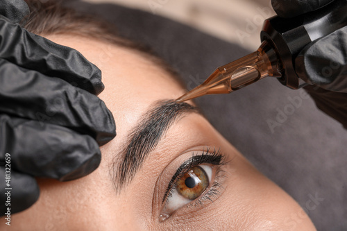 Foto Young woman undergoing procedure of permanent eyebrow makeup in tattoo salon, cl