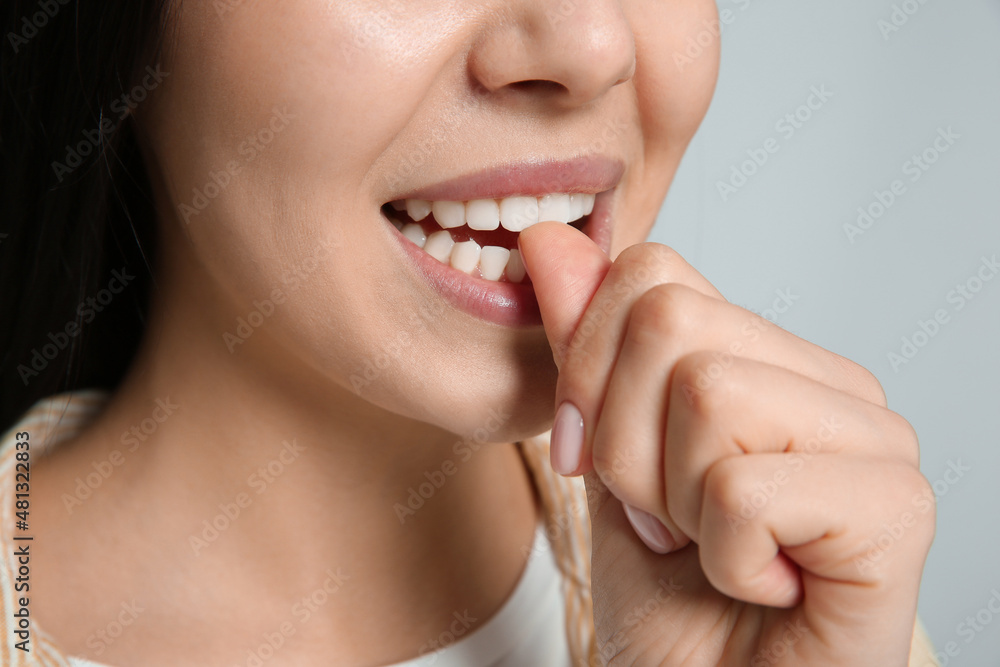 Young woman biting her nails on light grey background, closeup Young woman biting her nails on light grey background, closeup