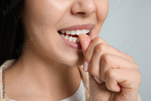 Young woman biting her nails on light grey background, closeup