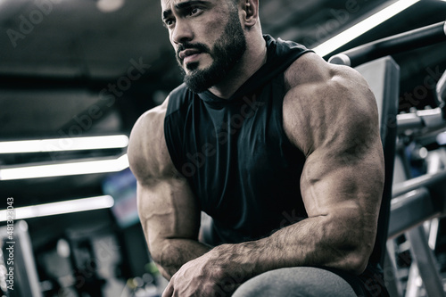 strong young bearded male sitting in sport gym during relaxing in muscle fitness training session