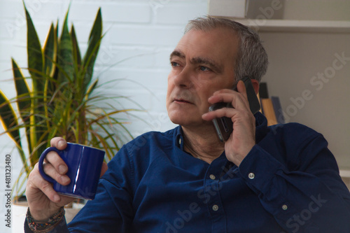 man at home with mobile phone or smartphone and cup of coffee