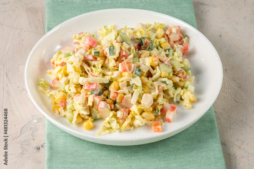 Homemade salad of crab sticks, cabbage, corn, served in a light plate, stands on a blue cloth, white table. Homemade salad of crab sticks, cabbage, corn, served in a light plate, stands on a blue cloth, white table.