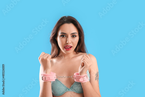 Young woman with handcuffs from sex shop on blue background