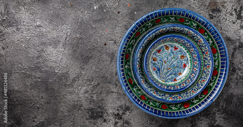 Three hand painted blue ceramic dishes, traditional Uzbek utensils dishes, bowl, plates with national floral ornament on dark background, Long banner format. top view