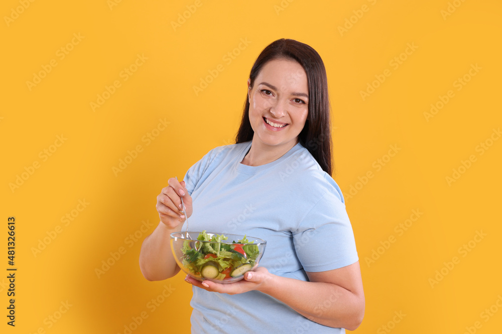 Beautiful overweight woman eating salad on yellow background. Healthy diet Beautiful overweight woman eating salad on yellow background. Healthy diet