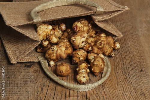 Jerusalem artichoke tubers in a burlap bag and wooden background.