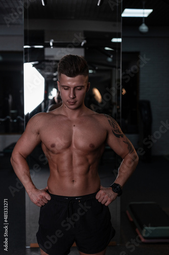 Strong handsome man bodybuilder trainer with hairstyle and naked sexy muscular body in the gym