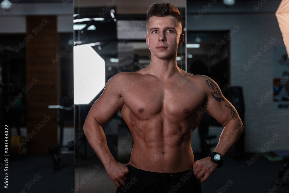 Bodybuilder man athlete with a bare muscular body and a tattoo posing in the sports gym