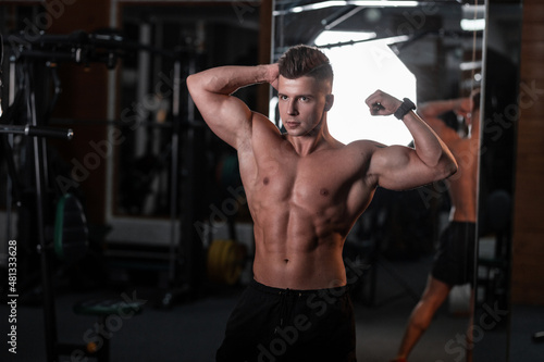 handsome young bodybuilder guy with a naked tanned torso trains in the sports gym