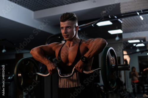 Handsome strong man trainer with a muscular body pumps muscles in the gym against a dark background