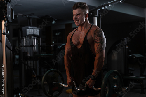 sports man bodybuilder with a muscular body in a black T-shirt expressively pumps his muscles and does an exercise in the gym