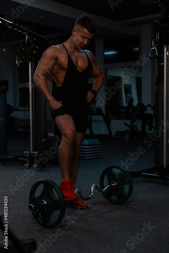 fitness trainer athlete guy with muscular body in black sportswear exercises in the gym on a dark background
