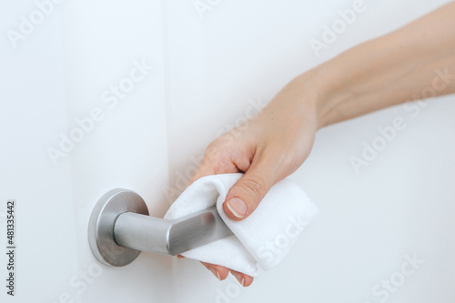 Cleaning door handles with an antiseptic wet wipe and gloves. Sanitize surfaces prevention in hospital and public spaces against corona virus. Woman hand using towel for cleaning home room door link.