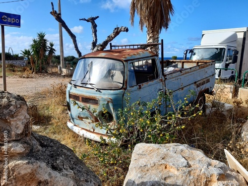 evocative image of an old rusty and abandoned van among brambles and boulders
 photo