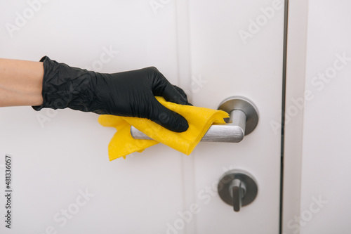 Cleaning door handle with yellow wipe in black gloves. Woman hand using towel for cleaning. Disinfection in hospital and public spaces against corona virus.