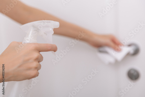 Cleaning white door handles with an antiseptic wet wipe and sanitizer spray. Disinfection in hospital and public spaces against corona virus. Woman hand using towel for cleaning home room door link.