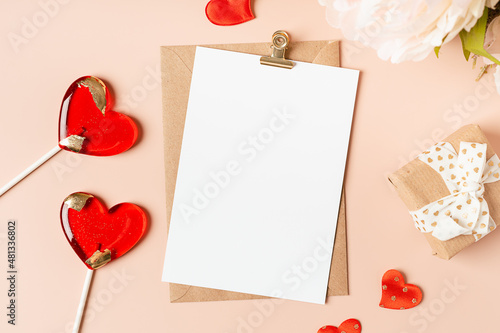 Flat lay of paper envelope with blank mockup greeting paper card. Pink table background with Valentine day gift, letter, heart shape, lollipops and decoration. Top view, mock up invitations