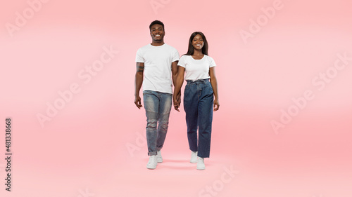 Confident couple walking to camera at pink studio background