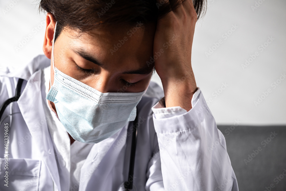 Depressed Young Asian male doctor with surgery face mask in a medical coat Overworked having a mental health breakdown during covid-19 outbreak. Medical and coronavirus Stress and frustration concept Depressed Young Asian male doctor with surgery face mask in a medical coat Overworked having a mental health breakdown during covid-19 outbreak. Medical and coronavirus Stress and frustration concept