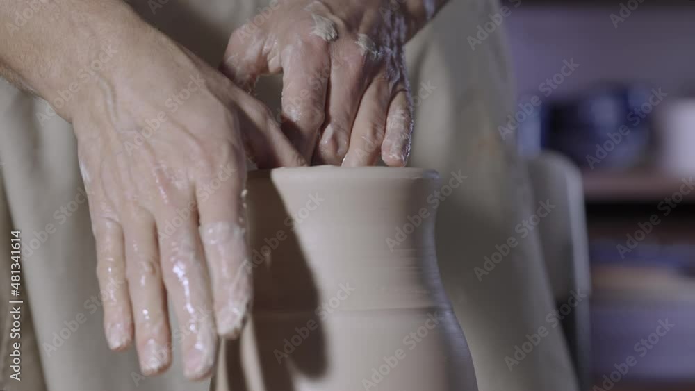 Male hands of a potter form a soft white clay pot neck, turning it on a potter's wheel in a creative workshop. The master gives a shape to the pottery. Clay shaping close up. Slow motion. Male hands of a potter form a soft white clay pot neck, turning it on a potter's wheel in a creative workshop. The master gives a shape to the pottery. Clay shaping close up. Slow motion.