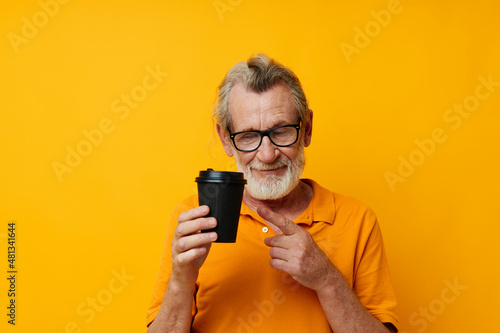 Senior grey-haired man with black disposable cup yellow background © Tatiana